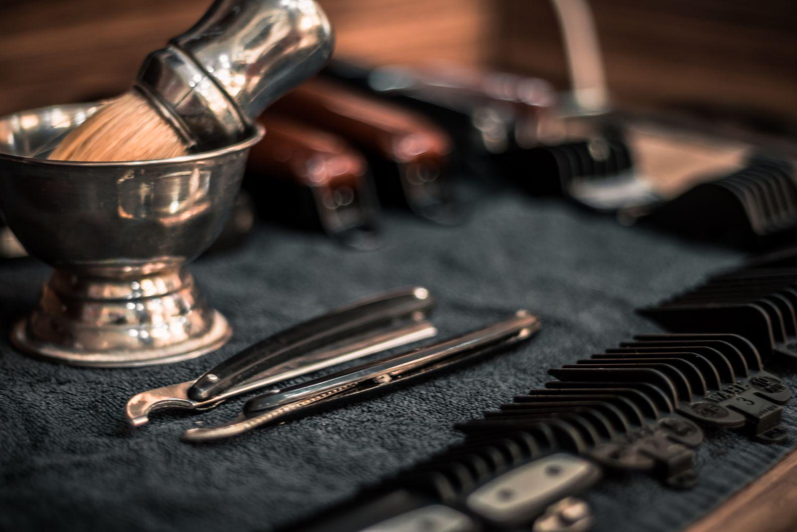 Straight razors, a shaving brush and clipper guards laid out on a towel