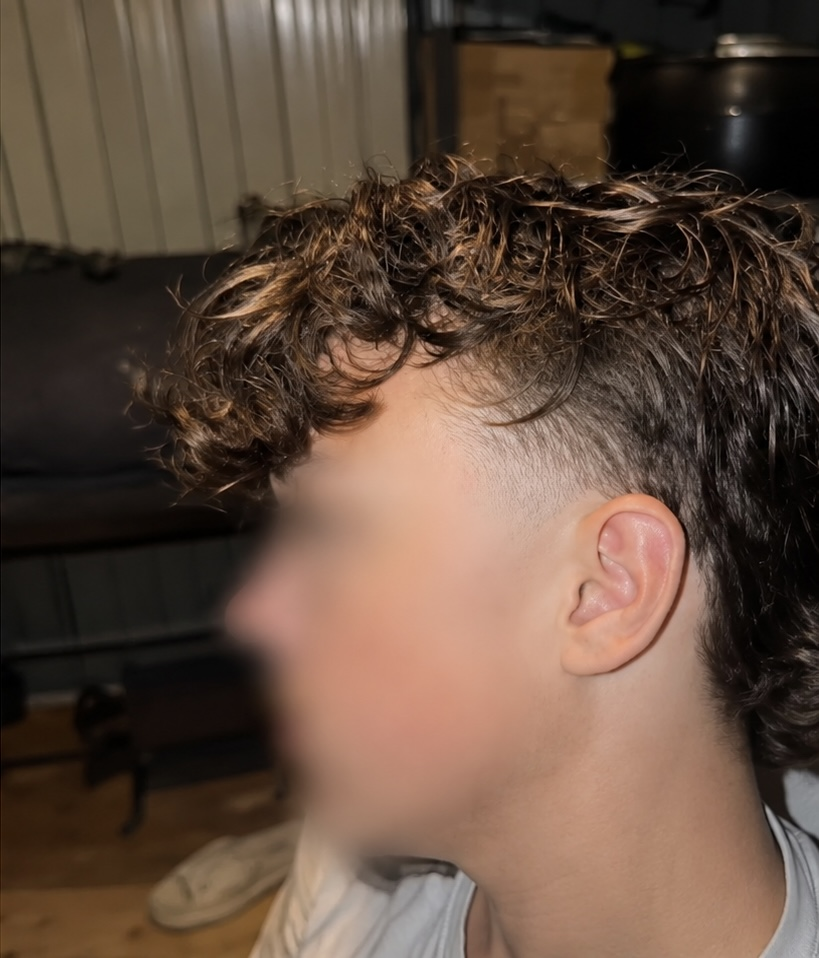 Loose curls left long on top with lightened ends, faded tight above the ear