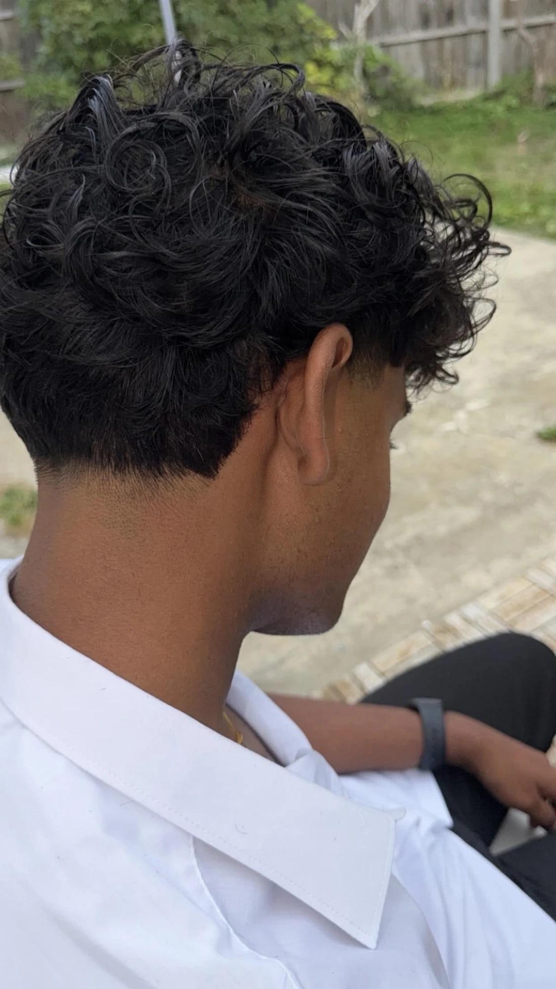 Loose curls left full on top, tapered low and clean at the nape